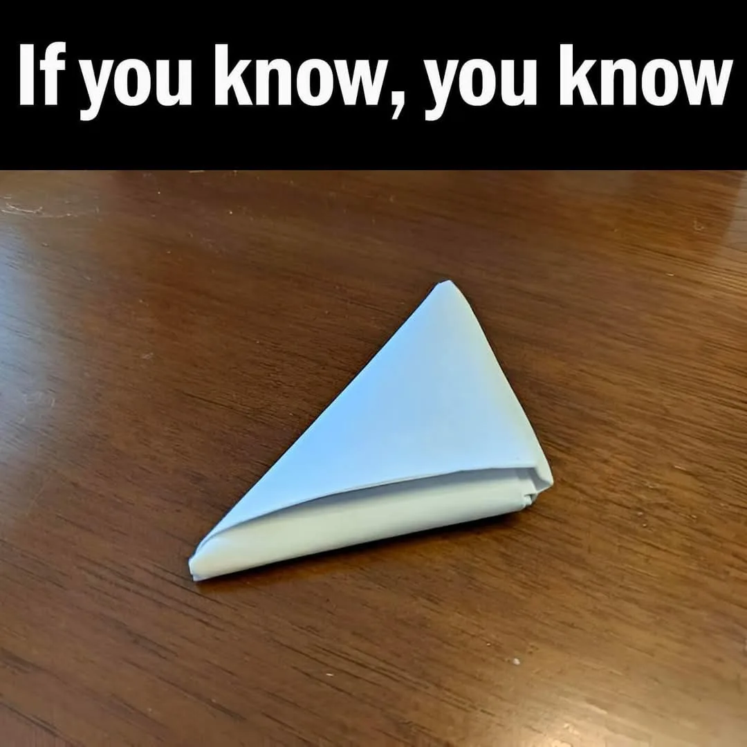 A white paper napkin folded into a triangular shape rests on a wooden table. The image has a black banner across the top…