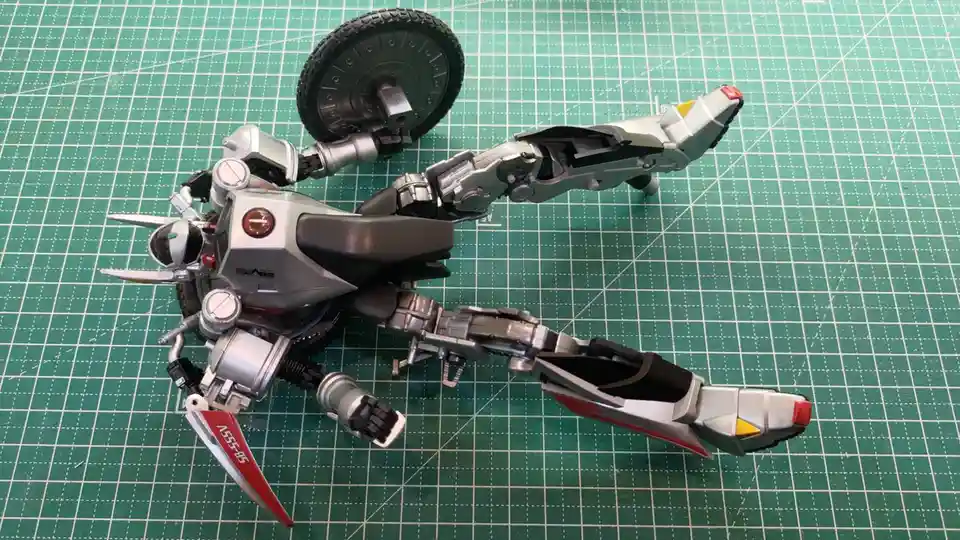 A silver and black robot model, resembling a motorcycle with articulated limbs and a large wheel, is posed on a green grid…