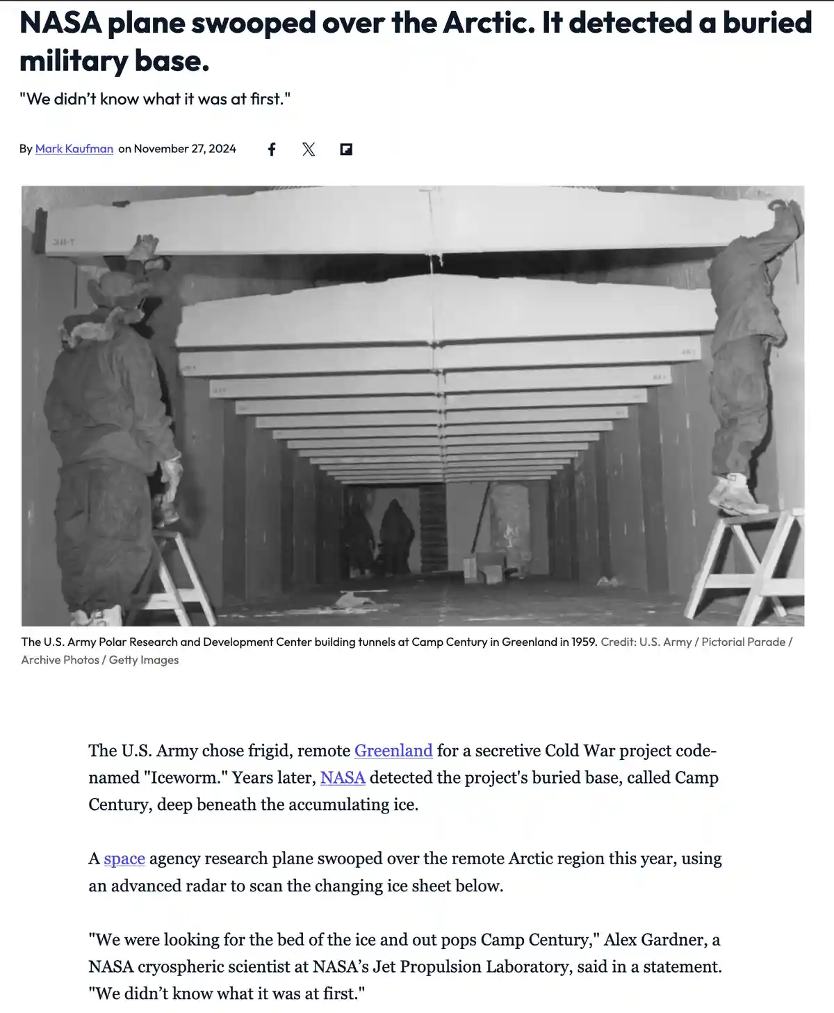 A black-and-white photo shows workers in heavy winter gear installing large, horizontal metal beams inside a long…