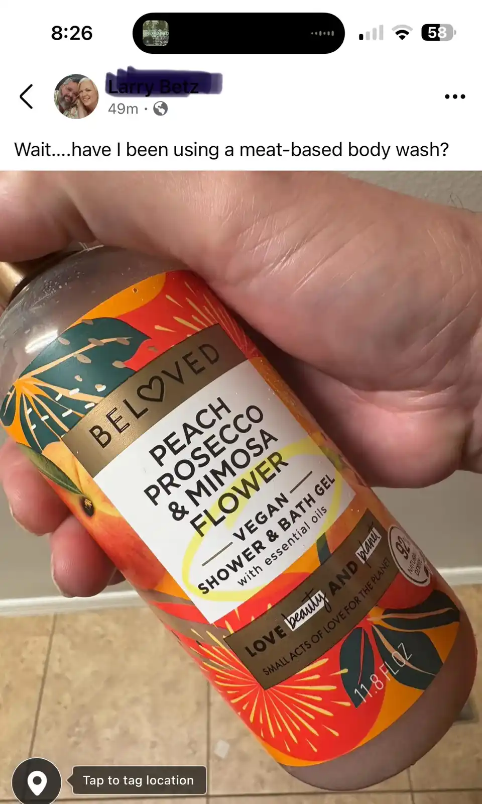A hand holds a bottle of 'Beloved' brand 'Peach Prosecco & Mimosa Flower' vegan shower gel, which clearly states it's vegan…