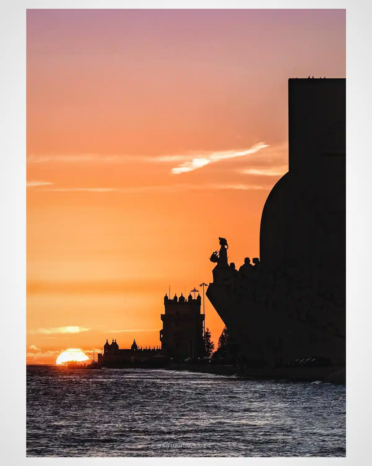 A scenic sunset photo of the Belém Tower and the Monument to the Discoveries in Lisbon, Portugal, silhouetted against an…