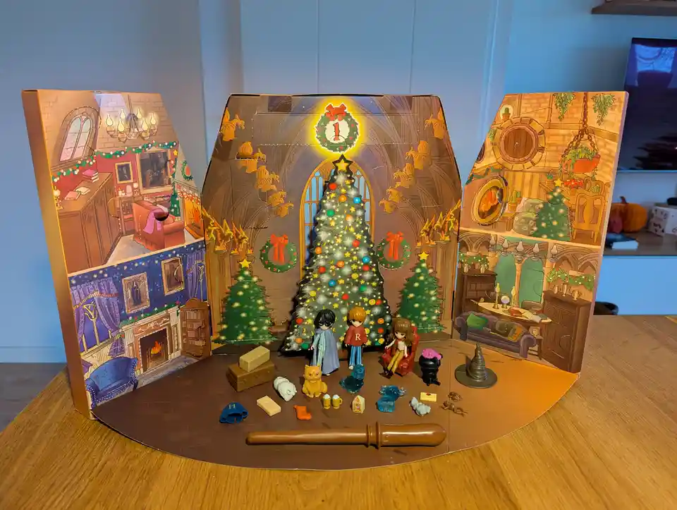 A Harry Potter-themed advent calendar is fully opened, revealing a festive scene with three illustrated rooms, a decorated…