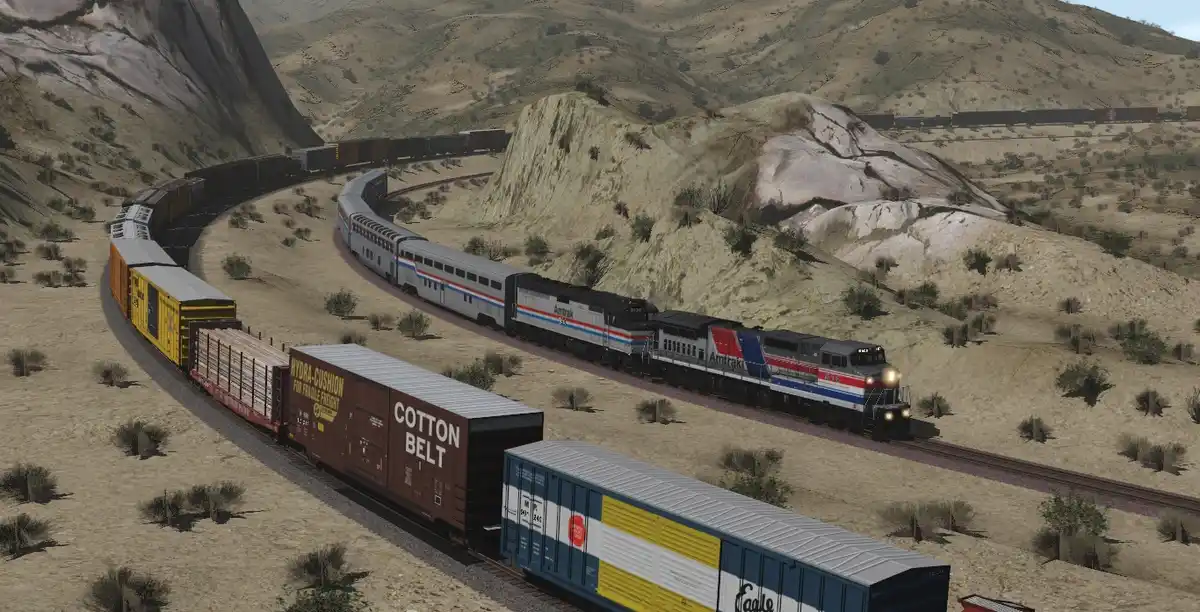 A screenshot from a train simulation game shows two trains on parallel tracks in a desert landscape. One is an Amtrak…