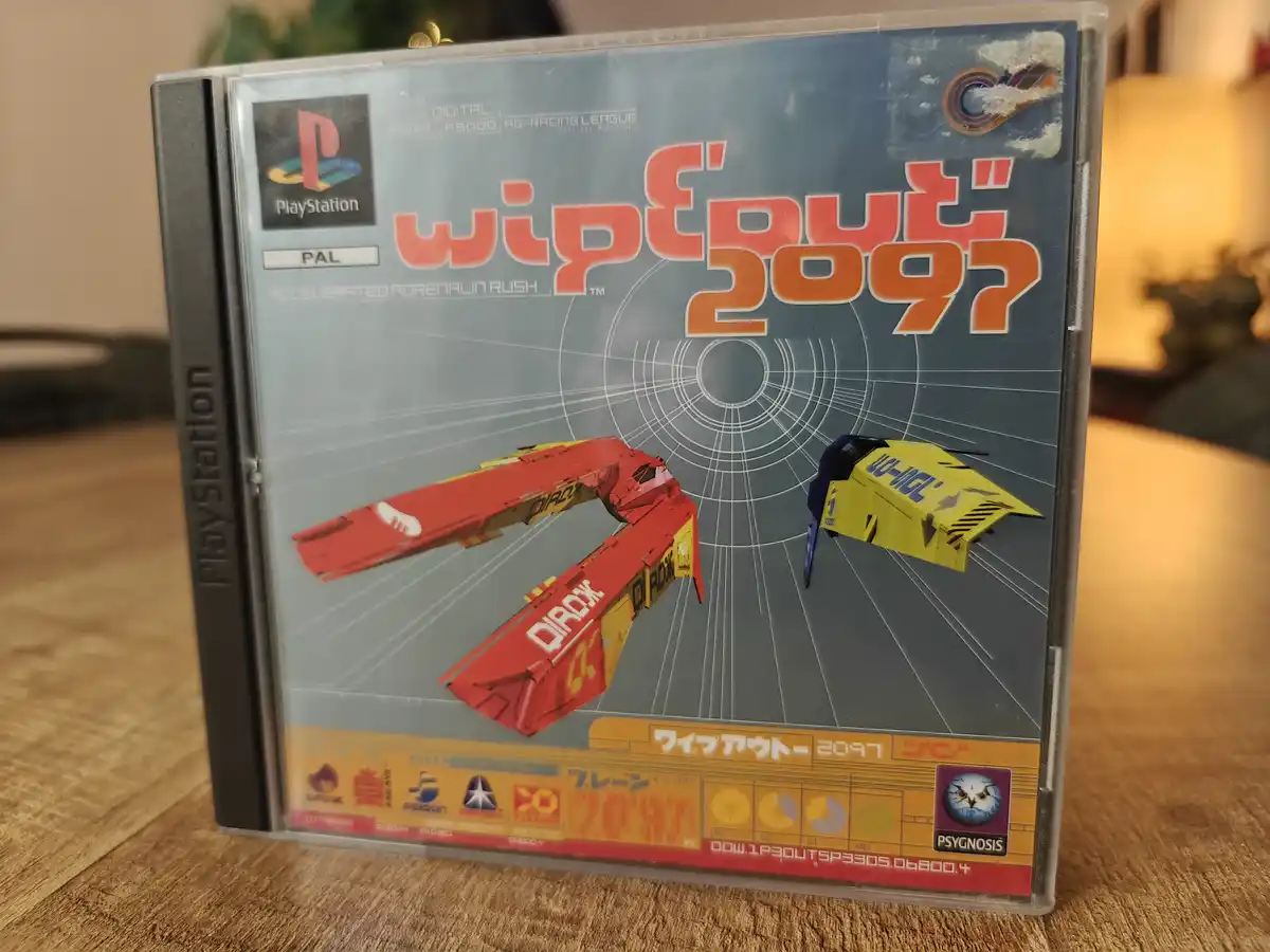A close-up photo of a PlayStation game case for 'Wipeout 2097', showing two futuristic racing pods on a grid background. The…