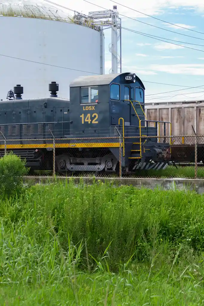 A dark blue diesel locomotive with the number 142 and the letters 'LOSX' painted in yellow on its side is parked behind a…