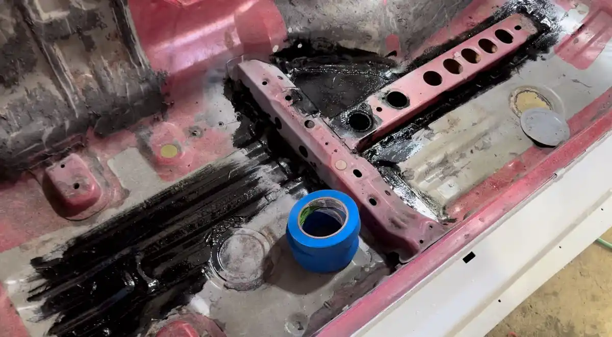 A close-up photo shows the interior of a car's engine bay with red-painted metal parts, black grease or paint splatters, and…