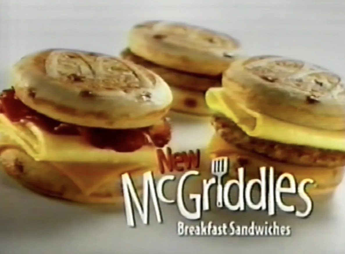 Three golden-brown McGriddles breakfast sandwiches are displayed on a white plate, each made with a griddle-marked circular…
