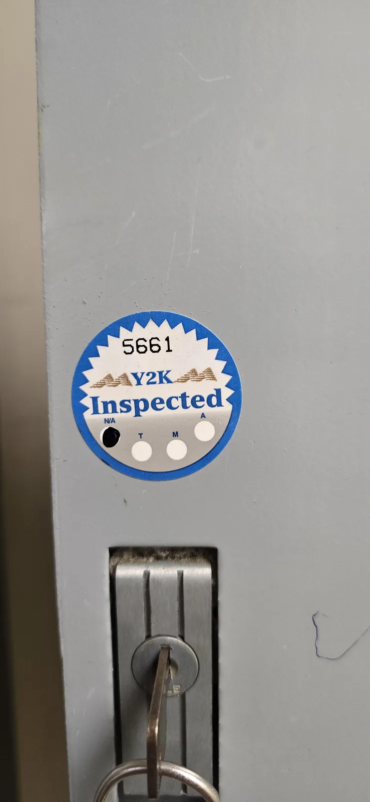 A close-up of a circular inspection sticker on a gray metal locker door, showing the number 5661, the text 'Y2K Inspected'…