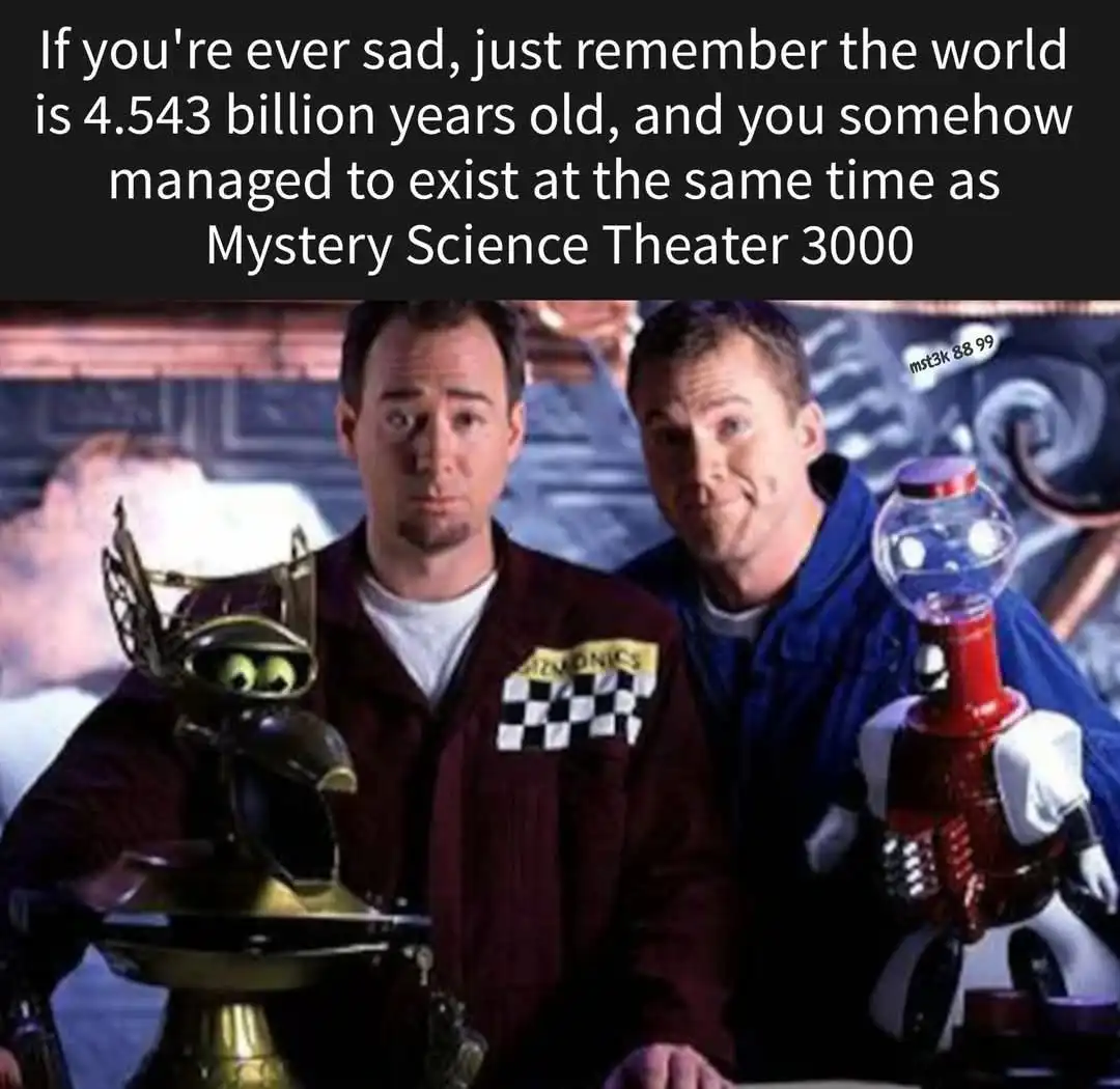 The image shows two men in lab coats standing beside robot-like figures, one holding a gumball machine. The text overlaid at…
