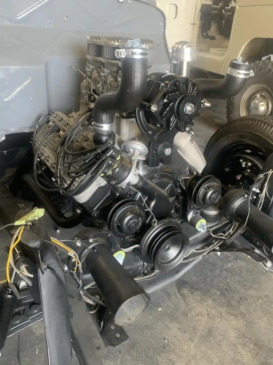 A close-up photo shows a complex, modified engine installed in a vehicle chassis, featuring black hoses, silver air filters…