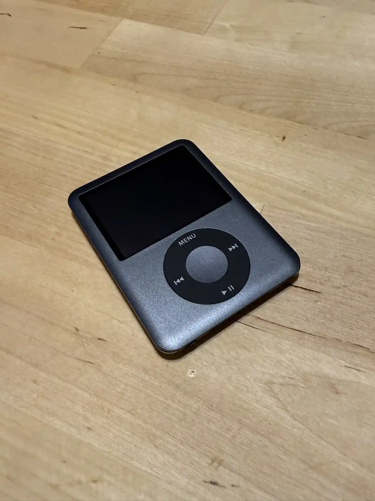 A silver Apple iPod classic with a black screen and circular click wheel rests on a light wooden surface. The device…