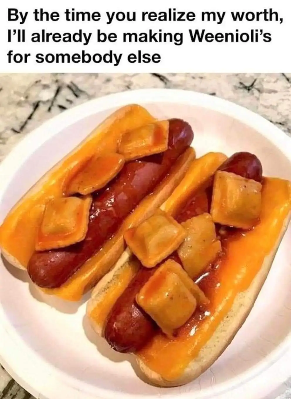 A white paper plate holds two hot dogs in buns, each topped with melted orange cheese and small, square, golden-brown fried…
