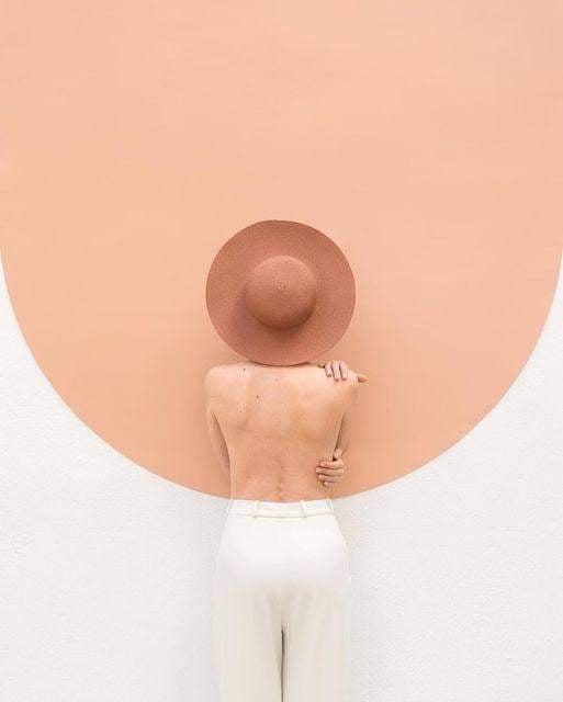 a person viewed from behind, wearing a wide-brimmed brown hat and white pants, stands with their back to the camera against…