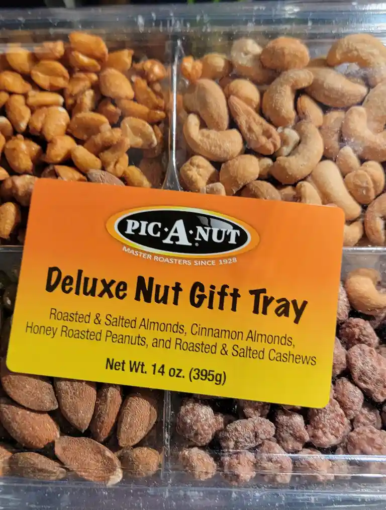 A close-up of a Pic-A-Nut brand 'Deluxe Nut Gift Tray' label on a clear plastic container holding four compartments of…