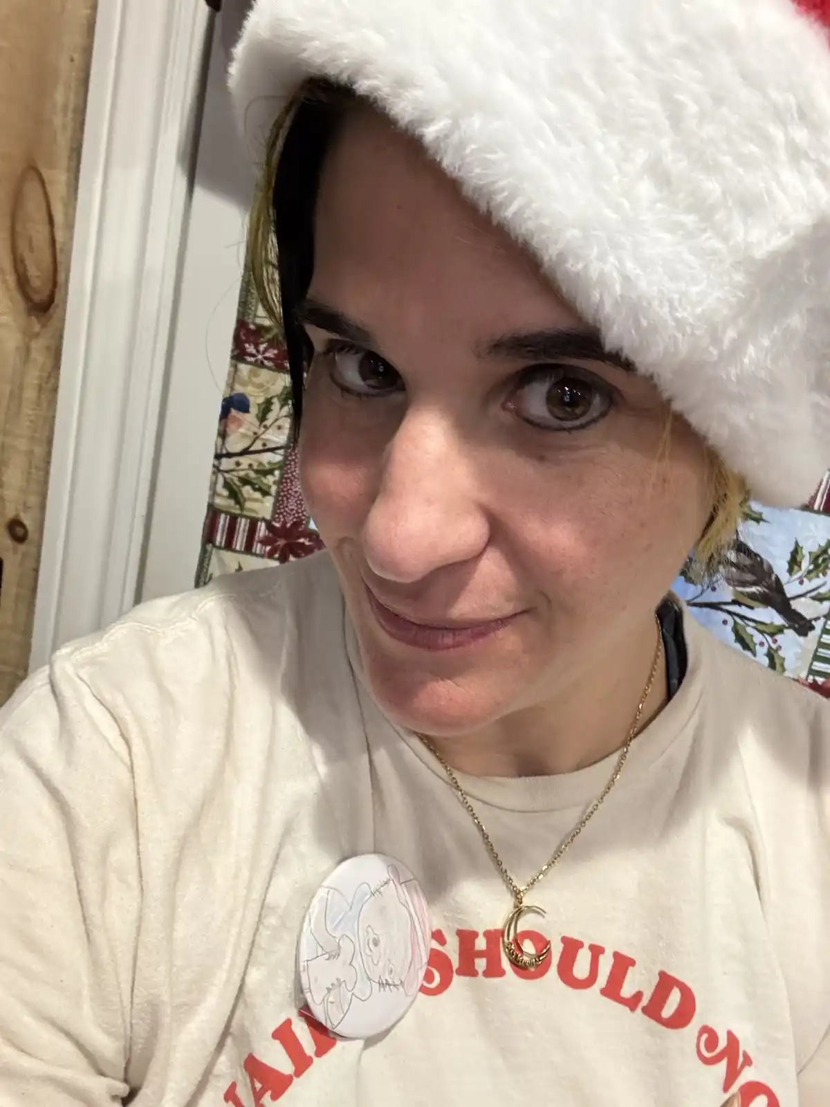 A person wearing a white fuzzy Santa hat and a cream-colored t-shirt with red text that reads 'I AM NOT A CHRISTMAS PERSON'…