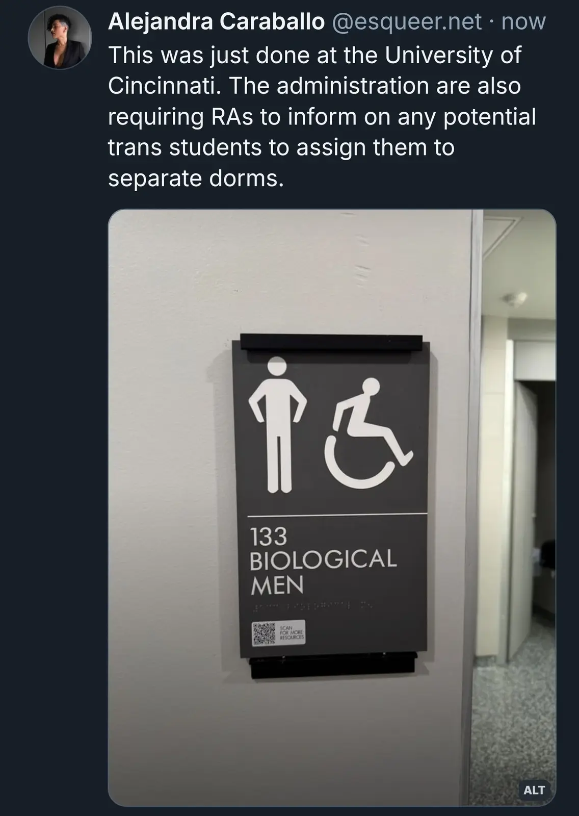 A dark gray restroom sign shows a male figure and a wheelchair symbol above the text '133 BIOLOGICAL MEN', with a QR code…
