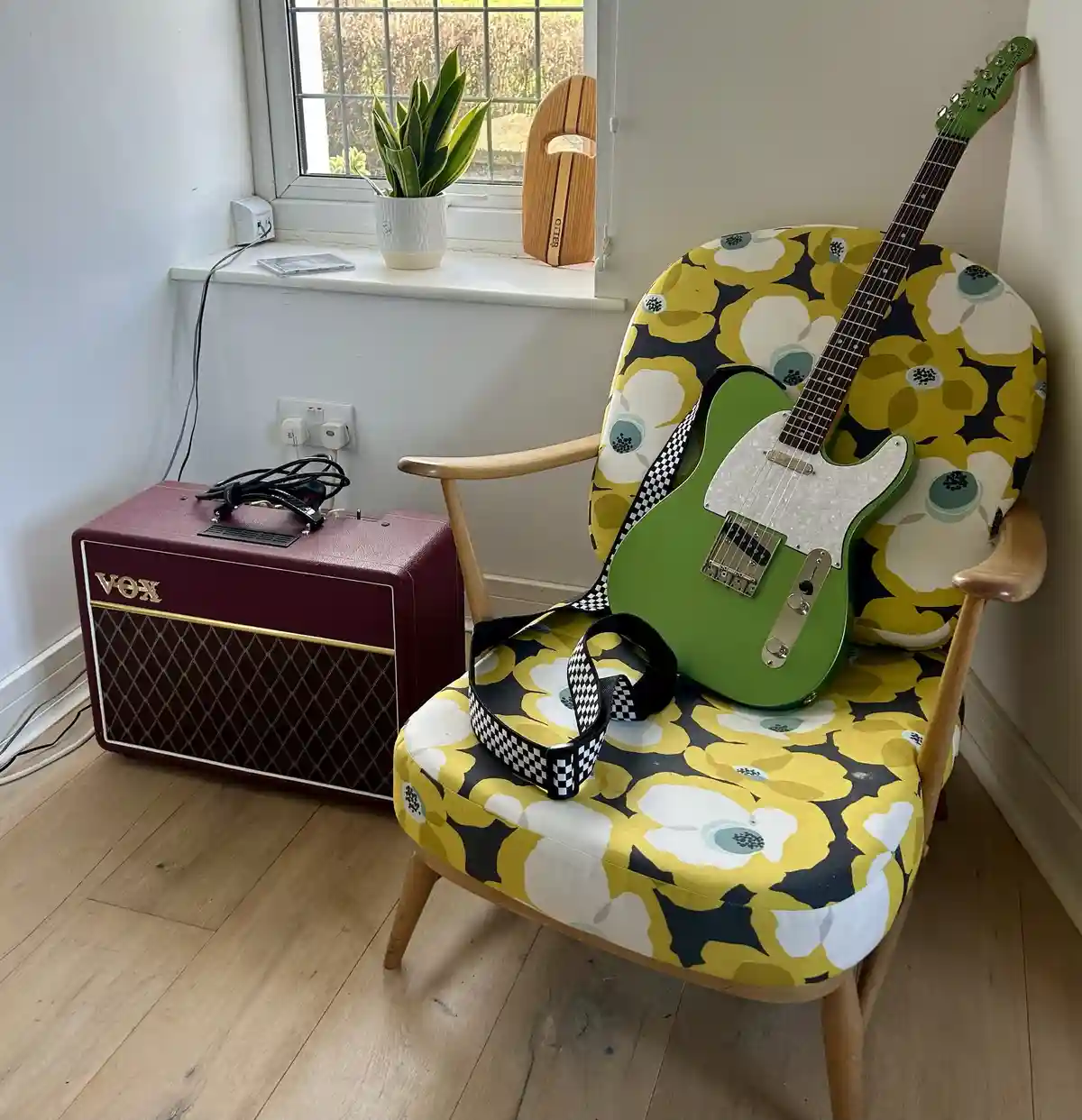 A green Fender Telecaster electric guitar with a black-and-white checkered strap rests on a yellow, black, and white…