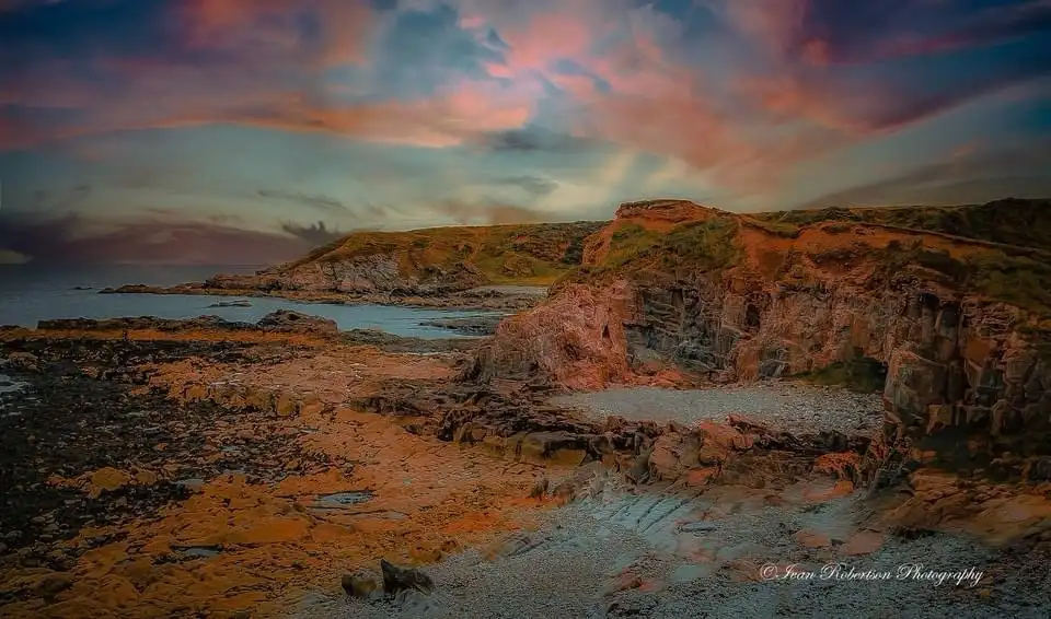A scenic photograph of a rocky coastline at sunset, with vibrant pink and orange clouds above rugged cliffs and pebbled…