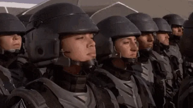 A still from the movie 'The Matrix' shows a line of identical-looking soldiers in black helmets and armor. The central…