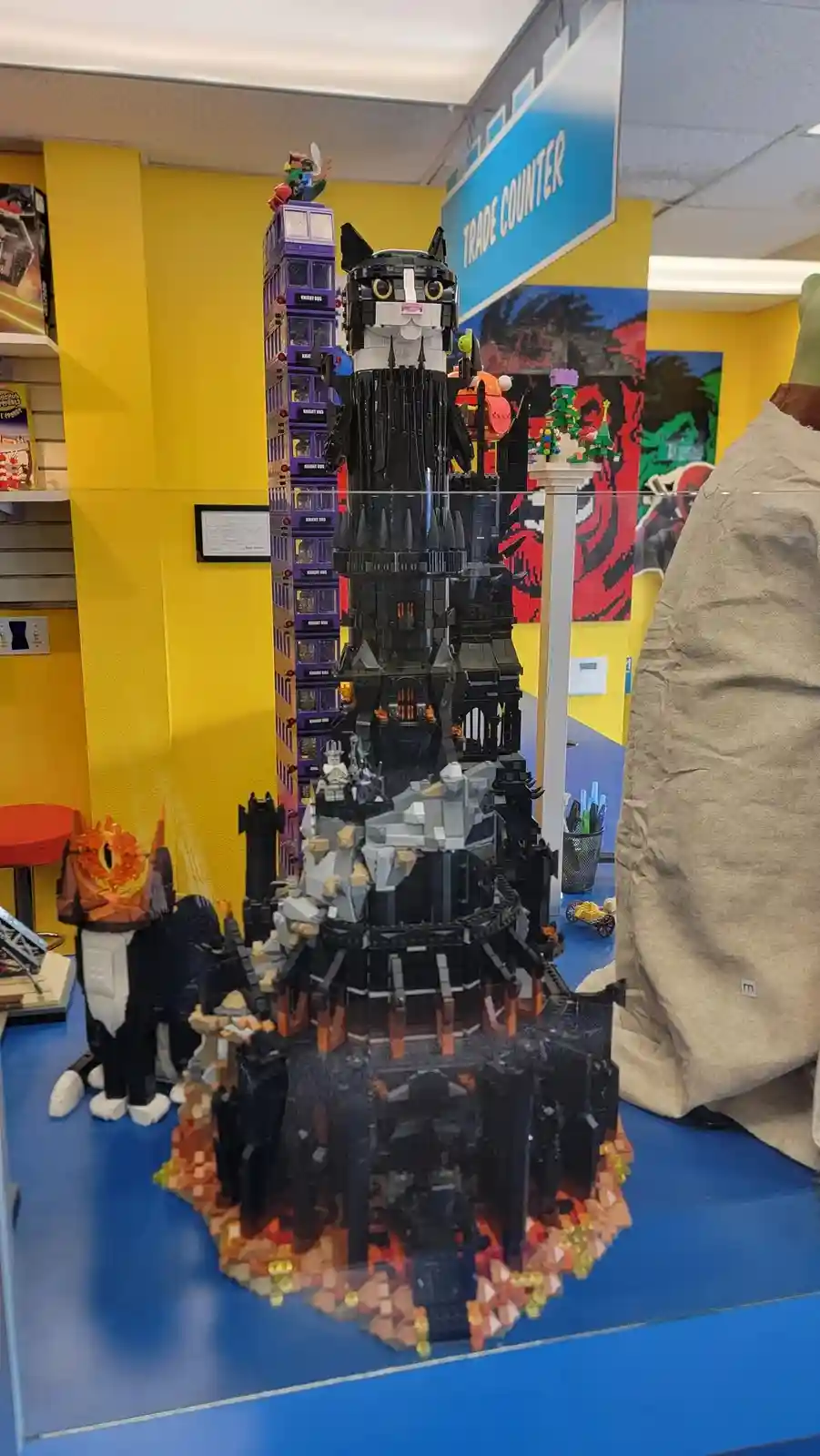 A large, intricate LEGO model of a dark, castle-like structure with a cat head at the top, displayed in a store with a…