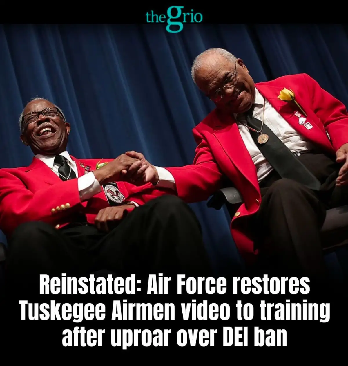 Two elderly Black men in red ceremonial jackets sit side by side, smiling and holding hands against a blue curtain backdrop…