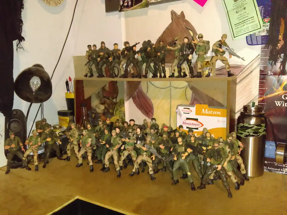 A large collection of military action figures, mostly in green and camouflage uniforms, are arranged on a wooden shelf and…