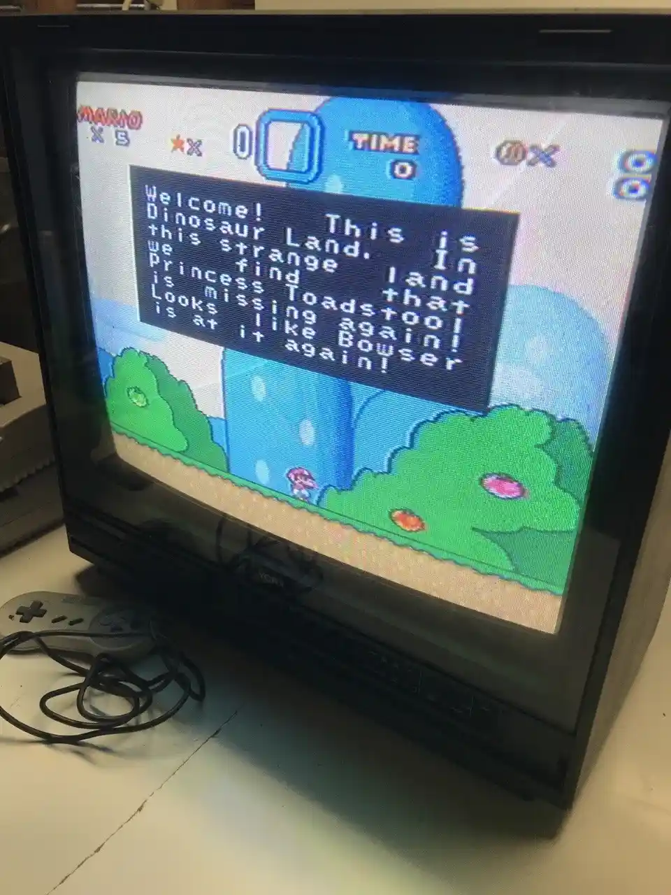 A photo of a CRT television displaying the intro screen of the Super Nintendo game 'Dinosaur Land,' which features a…