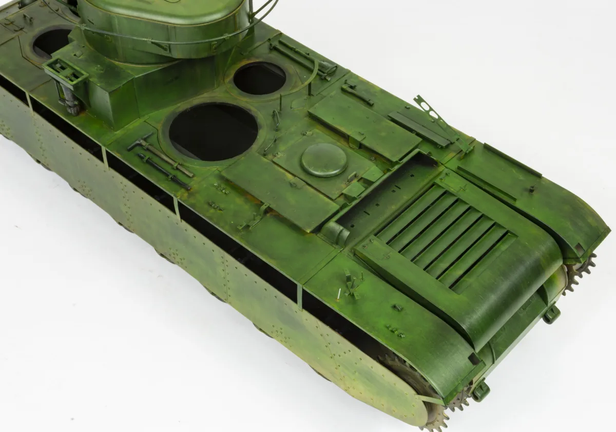 a green painted model of a tank is shown from a high angle against a white background, with visible rivets, hatches, and…