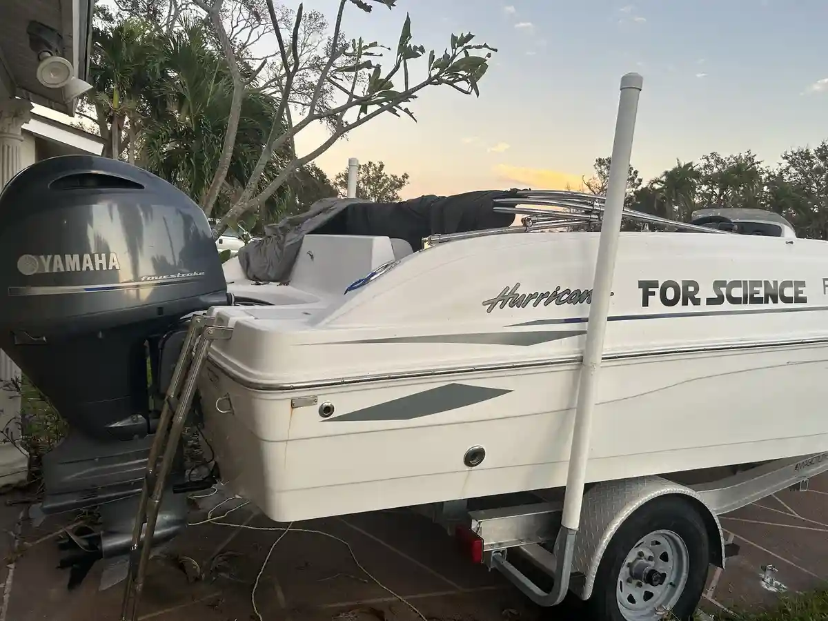A white motorboat with a Yamaha outboard engine is parked on a trailer in a driveway at sunset. The boat's side has…