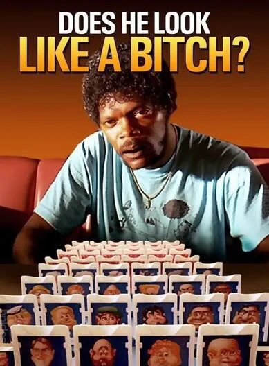 A man with curly hair and a light blue t-shirt sits at a table with a large pyramid of playing cards, each showing a…