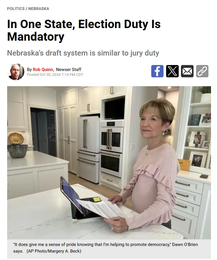A woman in a pink ruffled sweater stands in a modern kitchen holding papers while looking at a laptop. The image is a news…