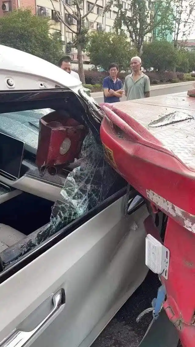 A silver car is severely damaged in a collision with a red vehicle, with shattered glass and crumpled metal visible. Three…