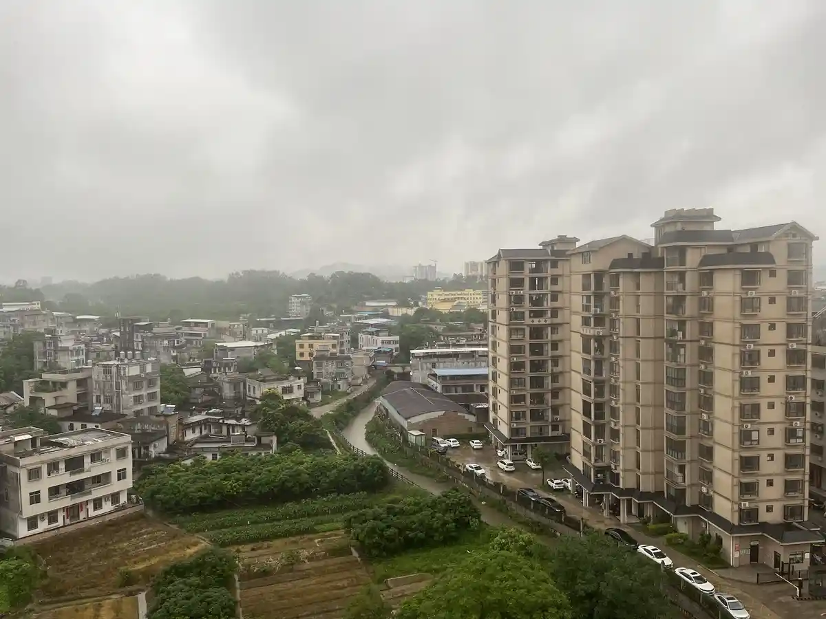 An aerial view of a mixed urban landscape under an overcast sky, showing modern high-rise apartment buildings alongside…