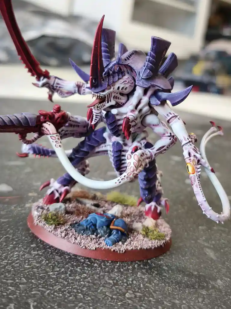 A highly detailed, painted miniature of a monstrous, multi-limbed alien creature with purple and white carapace, red horns…