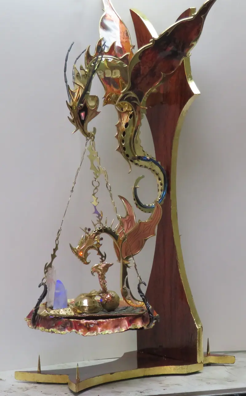 A decorative metal sculpture depicts two stylized dragons forming a balance scale, with one dragon's head and tail forming…