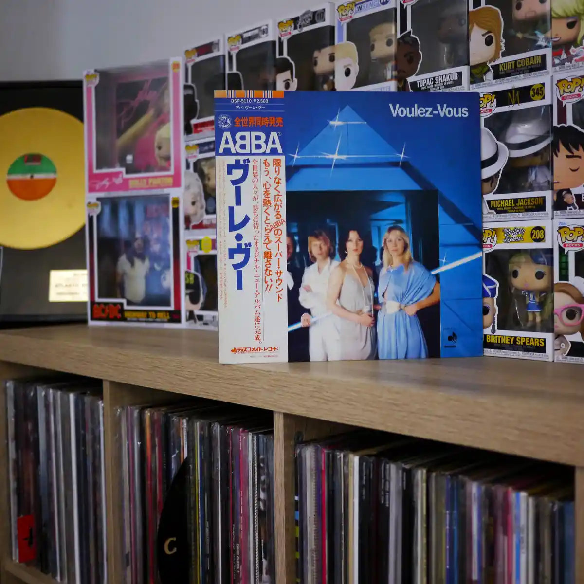A Japanese pressing of ABBA's 'Voulez-Vous' album cover is prominently displayed on a wooden shelf, surrounded by Funko Pop!…