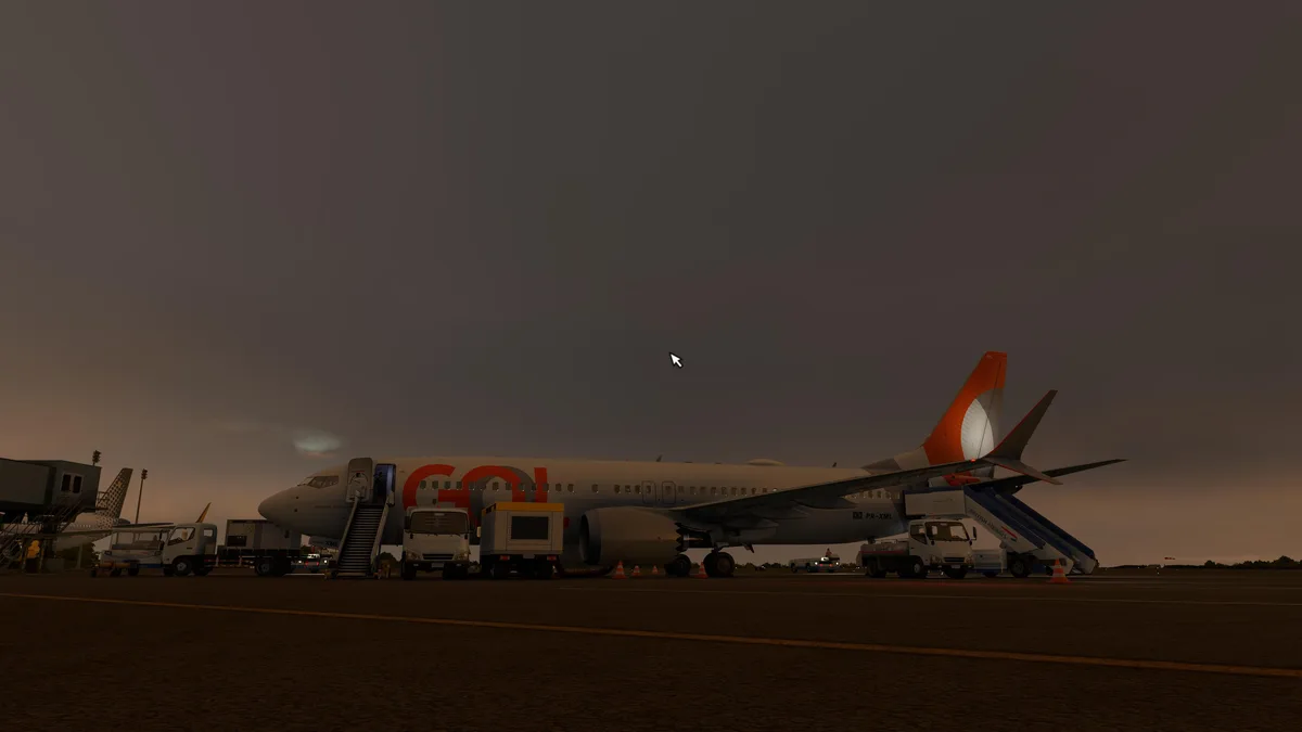 A dimly lit airport tarmac scene at dusk shows a GOL airline Boeing 737 parked with ground service vehicles and stairs. A…