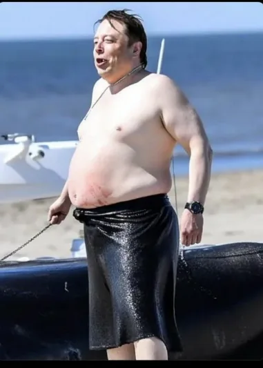 A shirtless man with a large belly stands on a beach next to a boat, wearing a shiny black skirt and holding a chain. The…