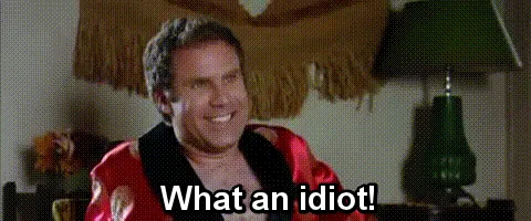 A man in a red robe laughs hysterically in a room with green lamps and a fringed curtain, with the text 'What an idiot!'…