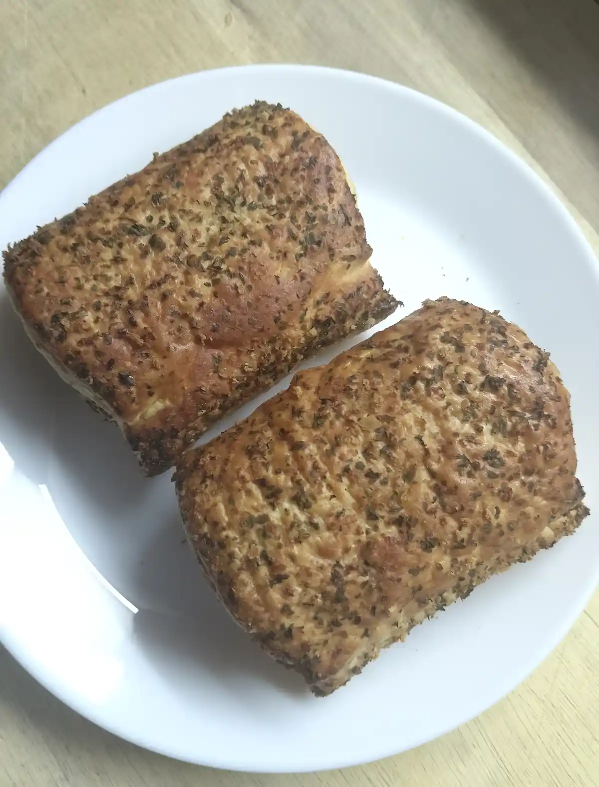 Two golden-brown, herb-topped bread rolls sit on a white plate atop a wooden surface. The overlaid text reads 'i made my own…