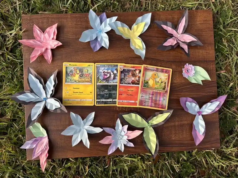 Four pokemon trading cards — Morpeko, Galarian Zigzagoon, Charmeleon, and Charmander — are arranged in a row on a wooden…