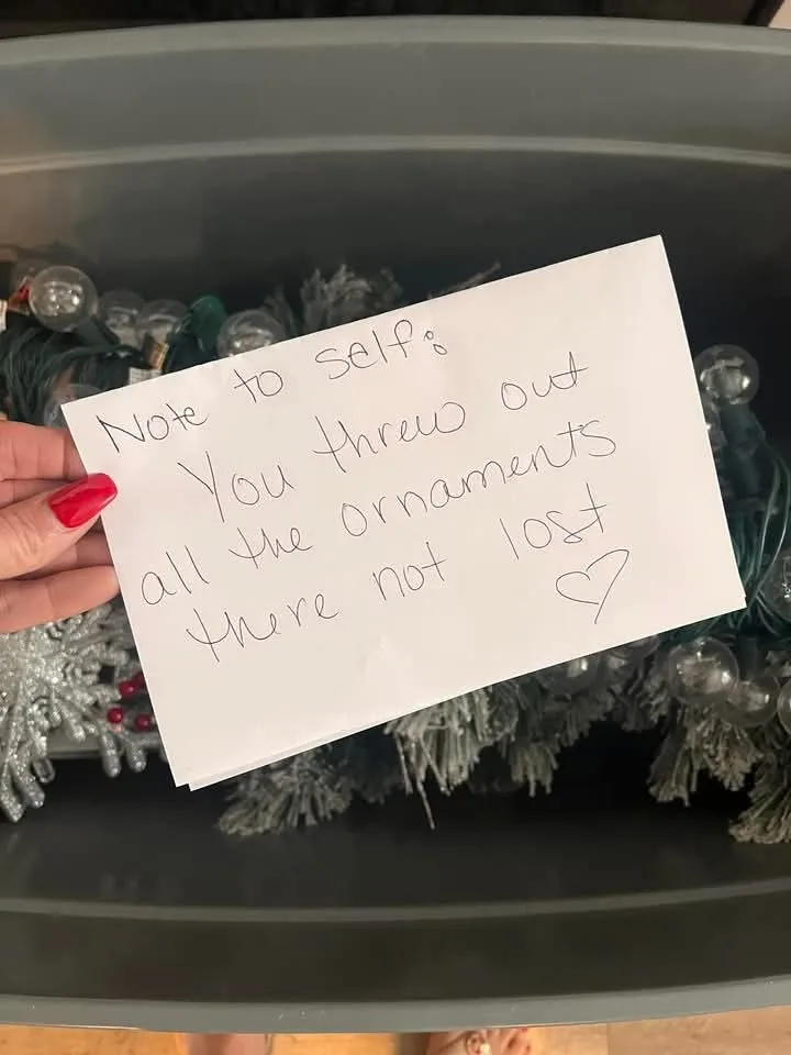 A hand with red nail polish holds a handwritten note that reads 'Note to self: You threw out all the ornaments there not…