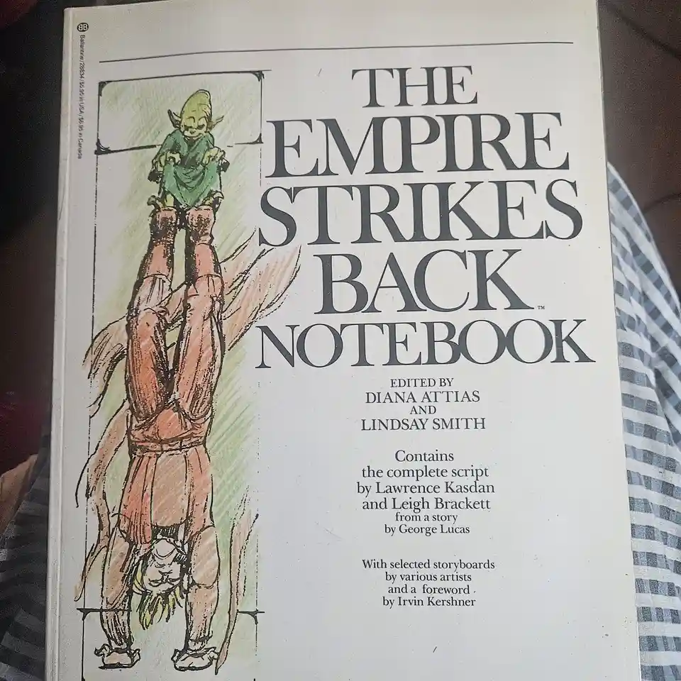 The image shows the cover of a book titled 'THE EMPIRE STRIKES BACK NOTEBOOK' with an illustration of a small green alien…