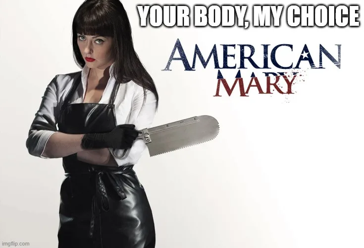A woman with dark hair and bangs, wearing a white shirt, black leather apron, and black gloves, holds a large handsaw with…