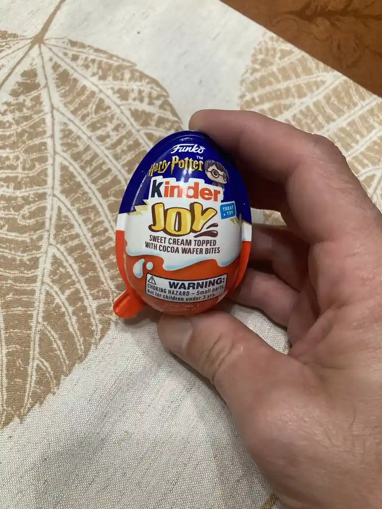 A hand holds a small Kinder Joy egg with Harry Potter and Funko branding, featuring a warning label about choking hazards…