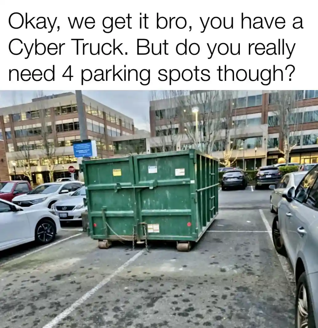 A large green dumpster is parked in a parking lot, occupying four marked parking spaces. Surrounding cars are parked…