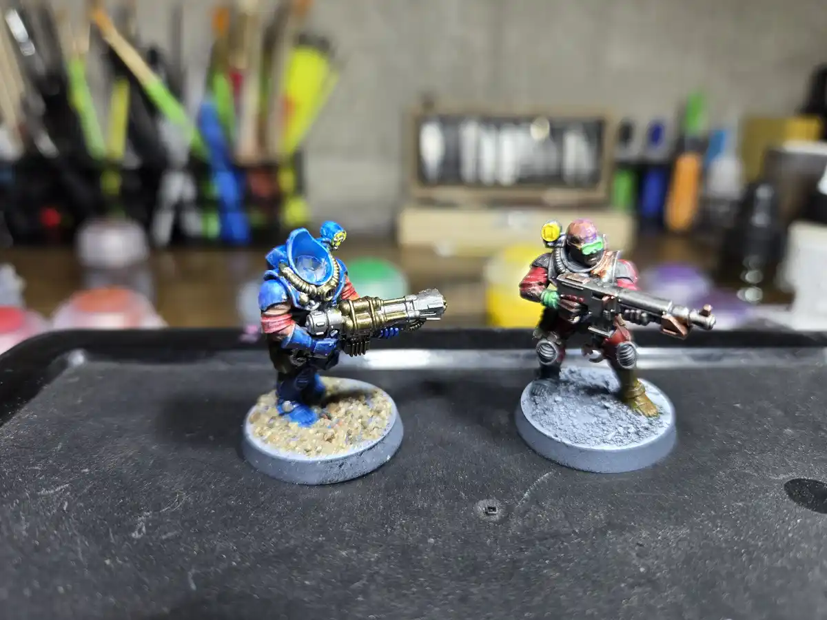 Two hand-painted miniature figurines, one blue and one red, stand on circular bases facing each other with weapons drawn…