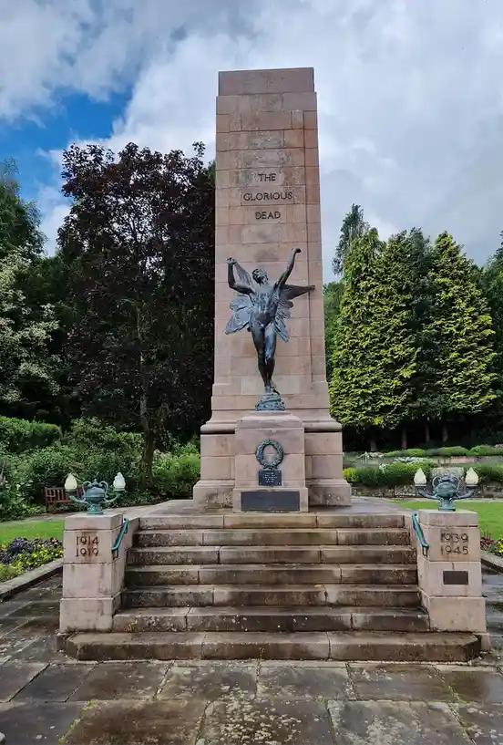 A tall stone war memorial with a bronze angel statue at its center, flanked by steps leading up to it. The memorial is…