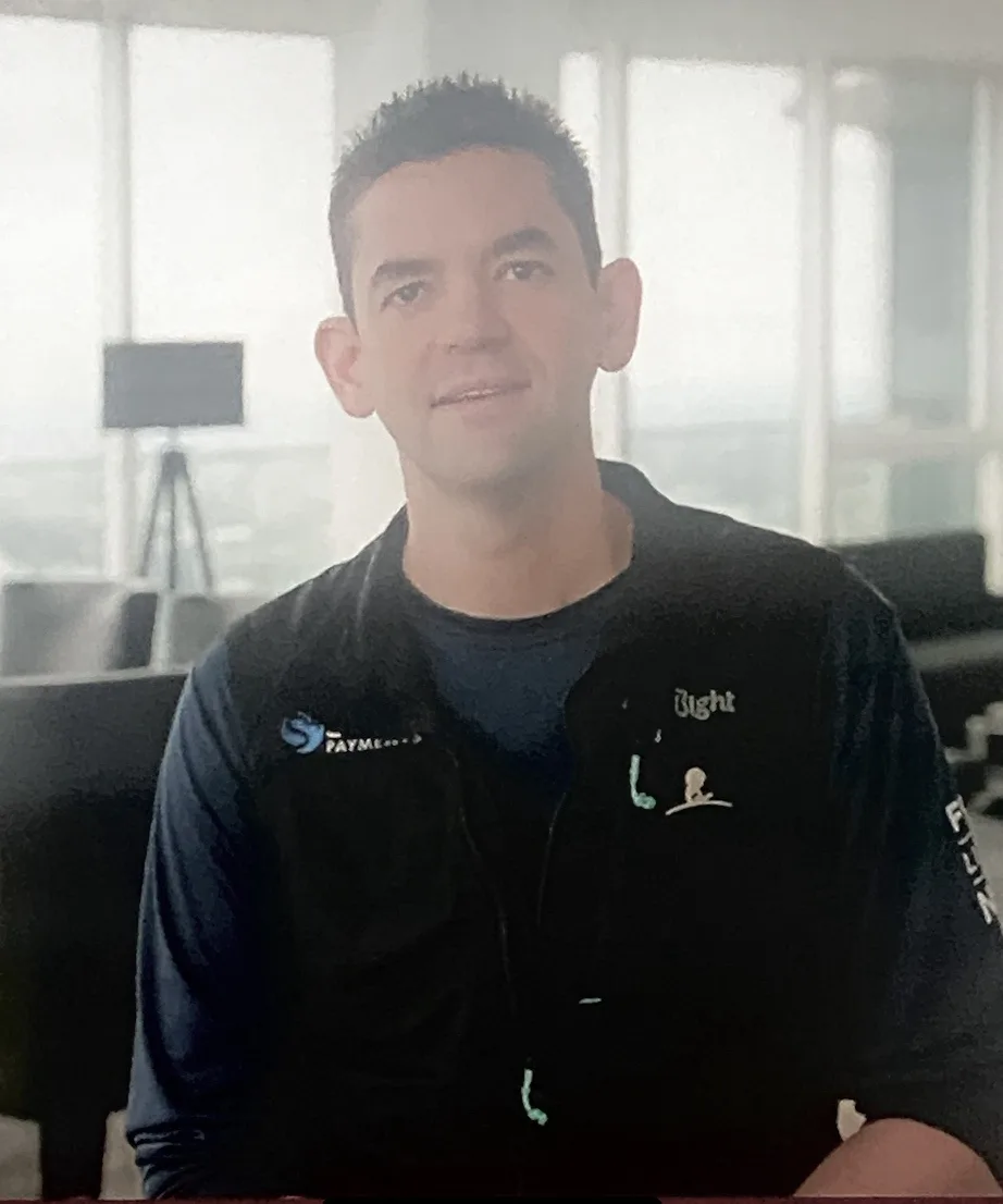 A man in a black jacket with 'PAYME' and 'Right' logos on it smiles at the camera. The image has been digitally altered with…