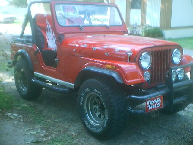 A red, modified Jeep Wrangler with a flame decal on the driver's seat and a red license plate that reads 'FEAR THIS'. The…